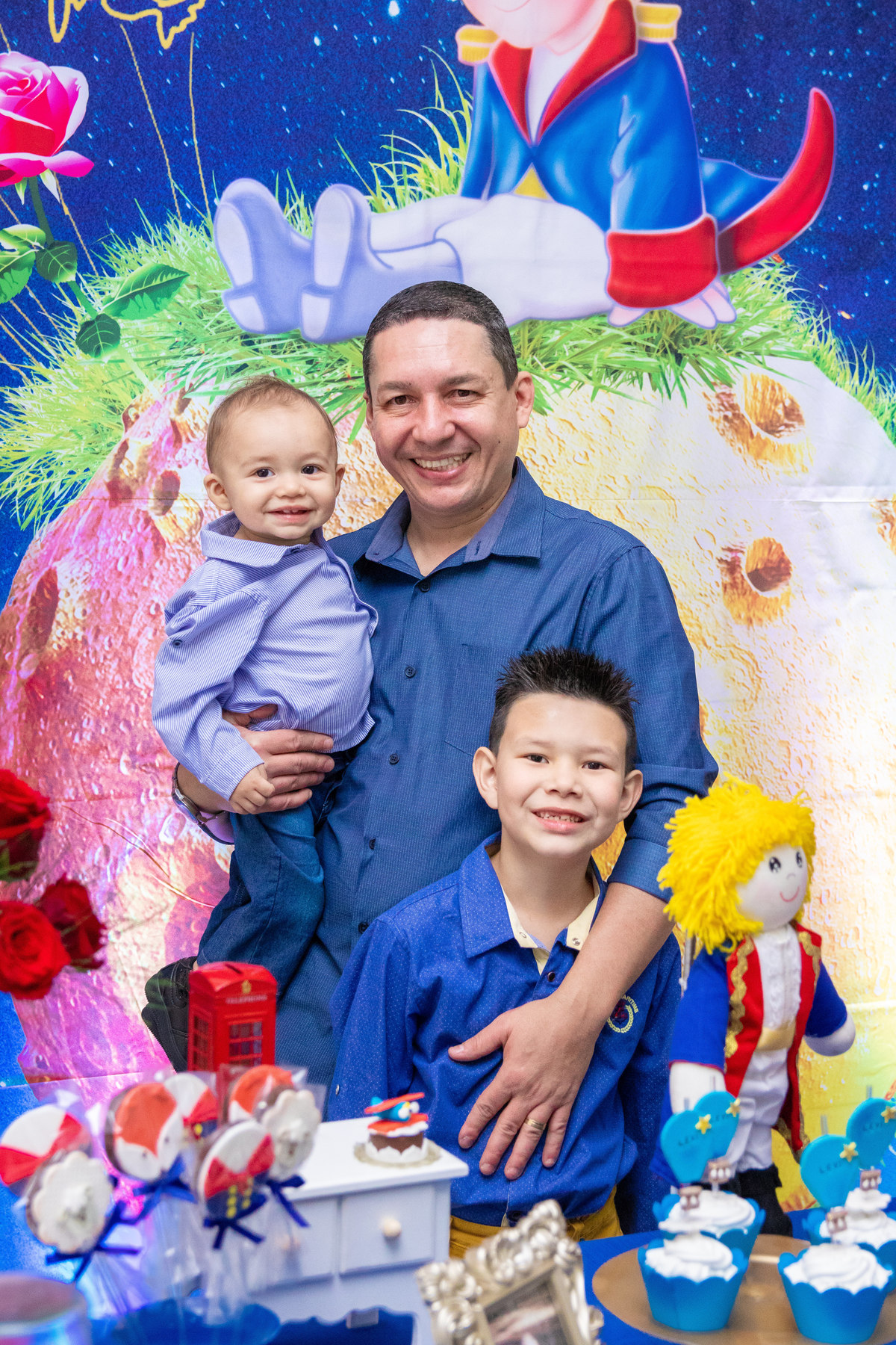 Aniversariante com seu pai e irmão na mesa do bolo