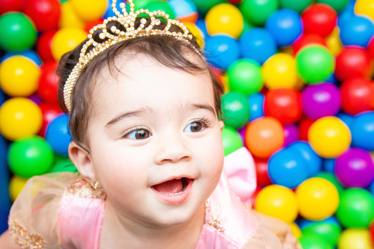 nenê com roupa de princesa e coroa brincando na piscina de bolinhas