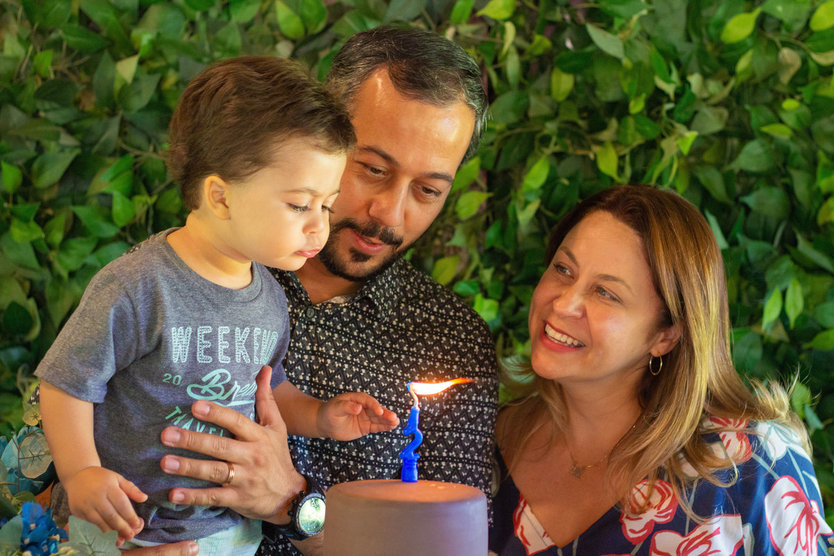 Mãe, pai e filho na mesa do bolo assoprando as velinhas