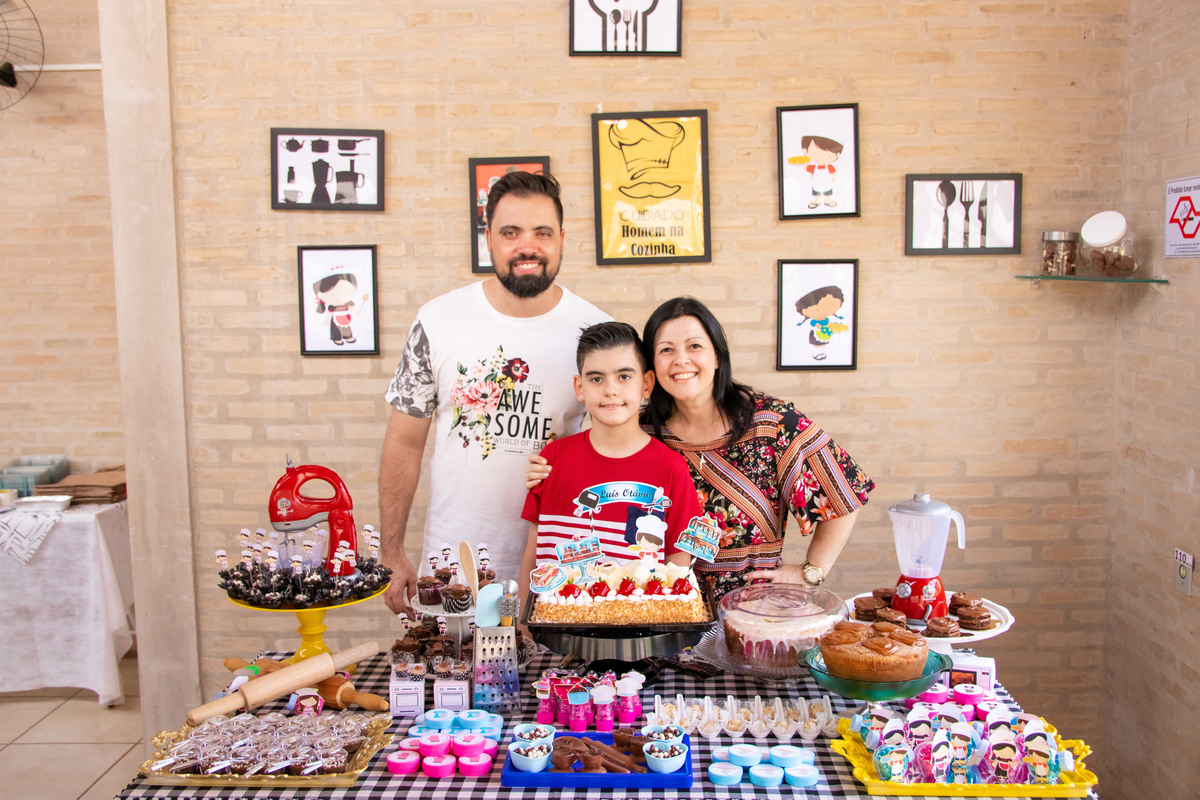 Aniversariante e seus pais na mesa do bolo