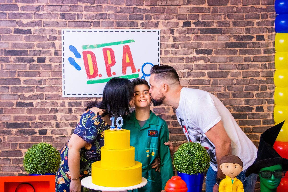 Aniversariante e seus pais na mesa do bolo