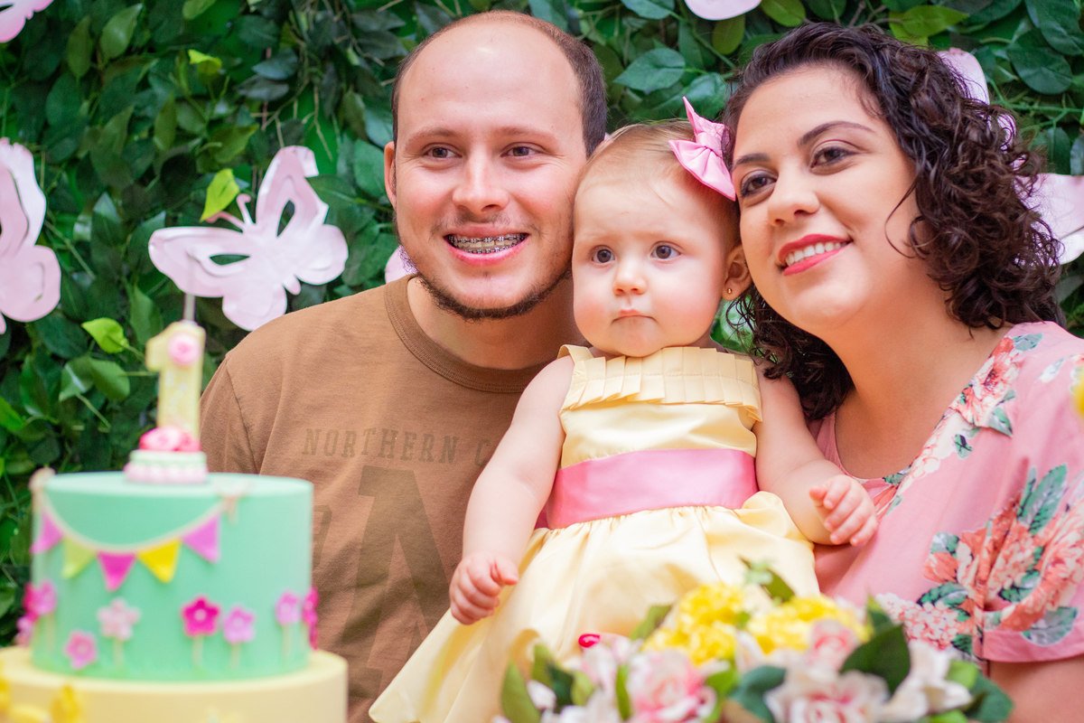 Aniversariante e seus pais na mesa do bolo