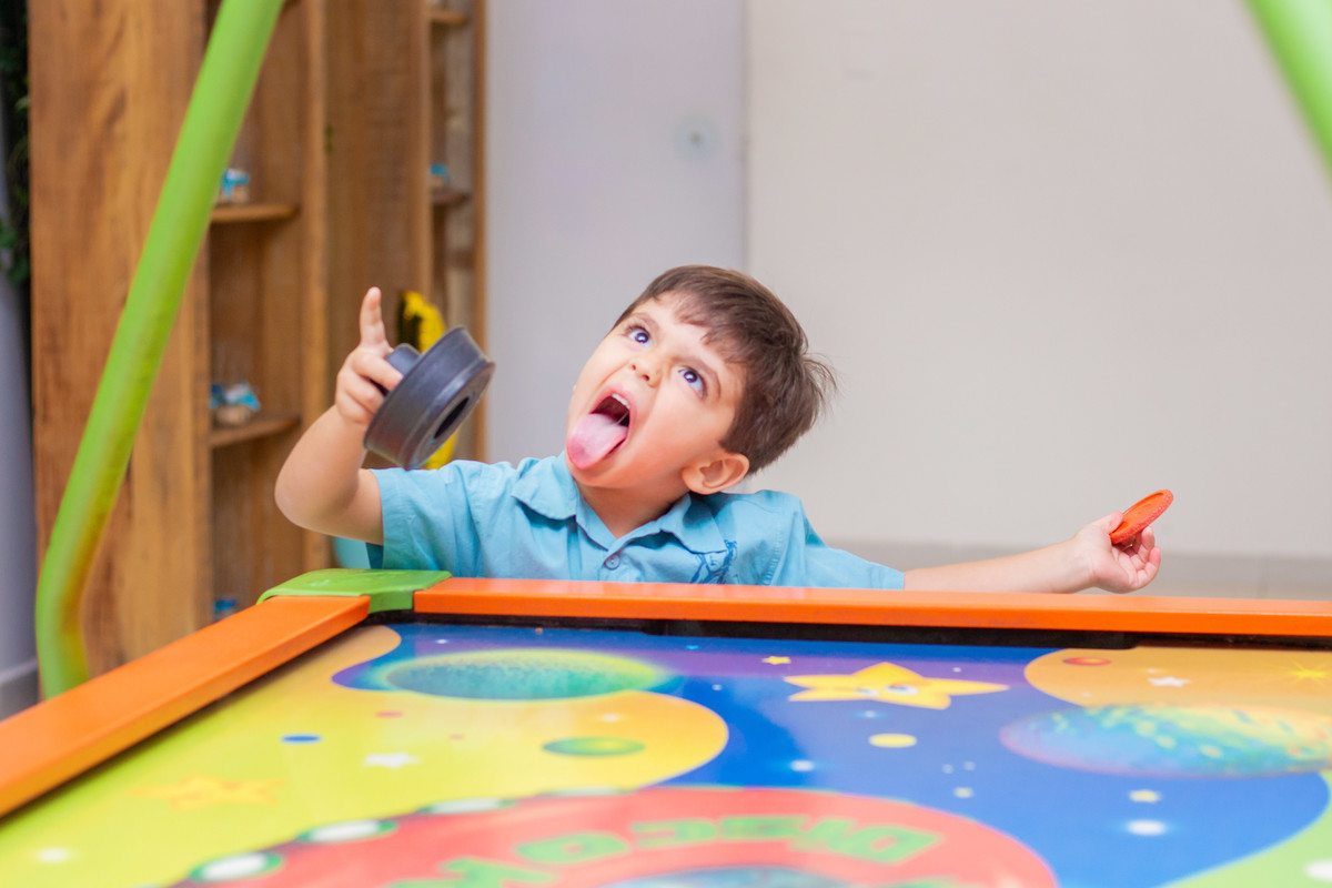 menino brincando no air hockey e fazendo careta