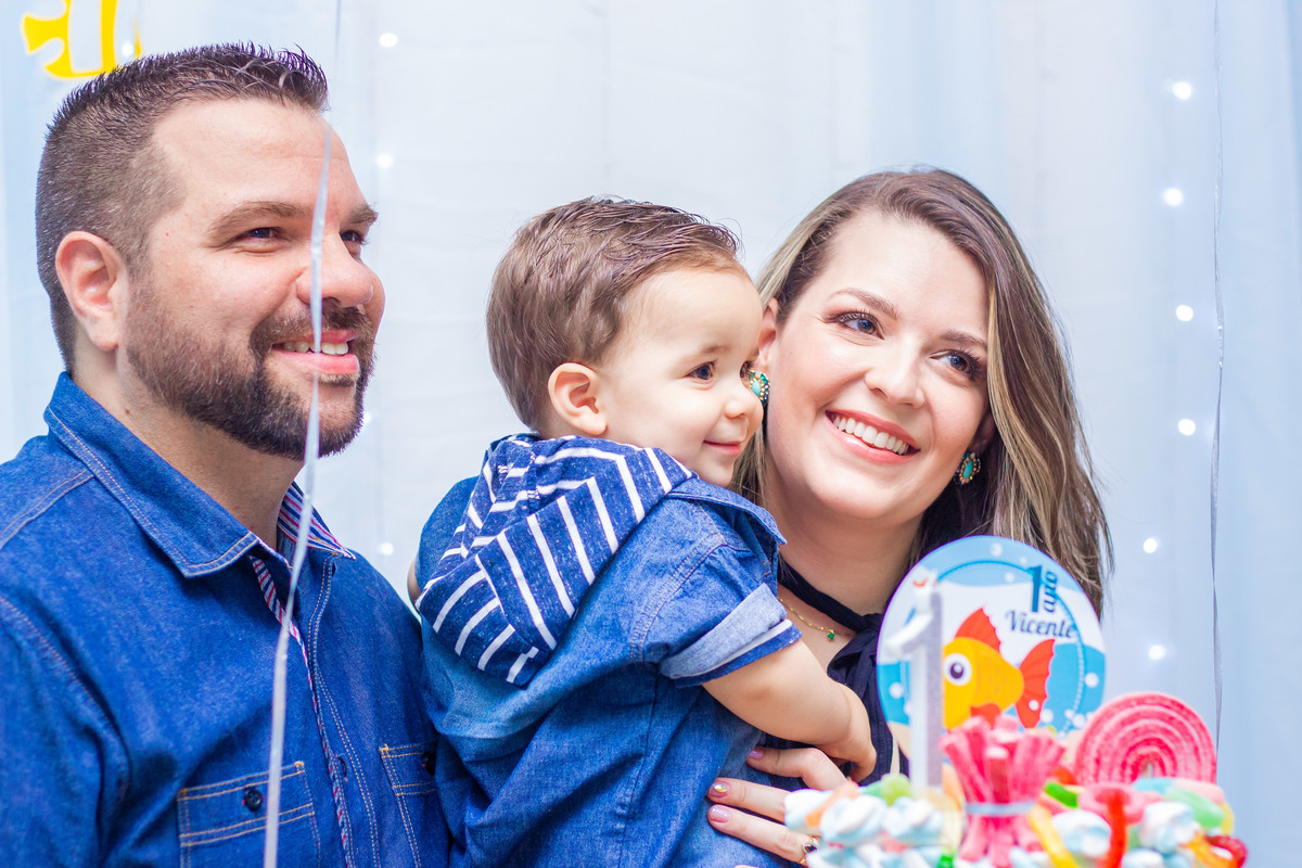 Aniversariante e seus pais na mesa do bolo