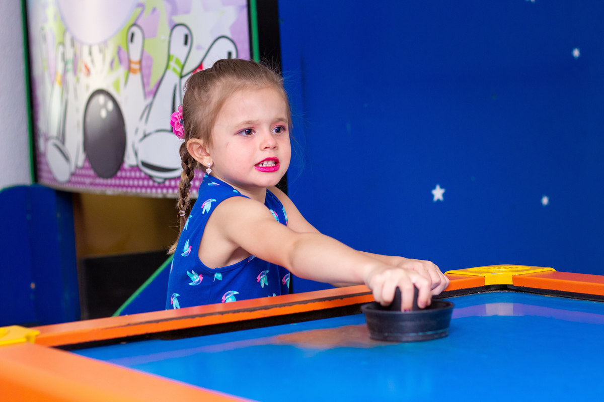 menina de vestido azul brincando no air hockey