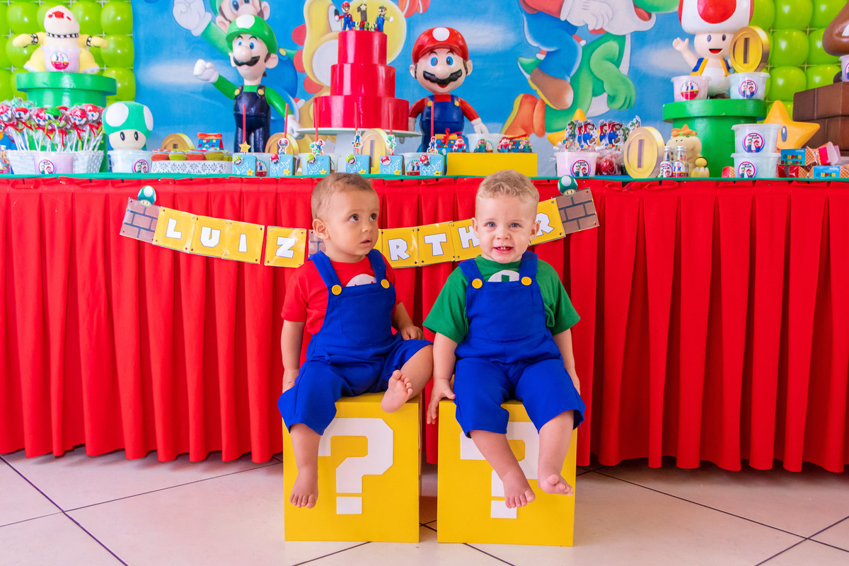 Foto com irmãos na mesa do bolo, foto de gêmeos em aniversário, fantasia Mario Bros em nenê de 1 ano