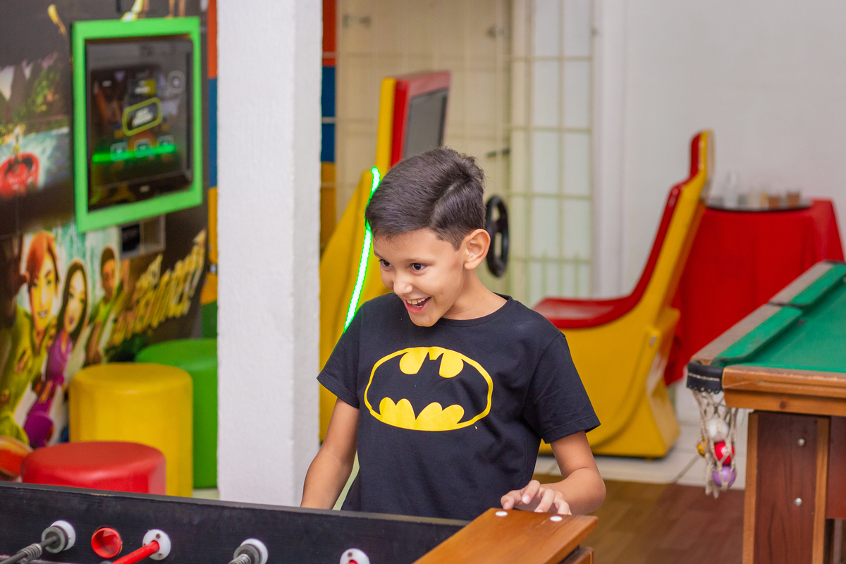 menino vestido de batman brincando de pebolim