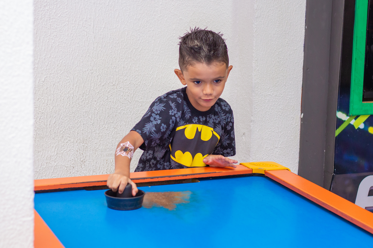 menino vestido de batman jogando air hockey