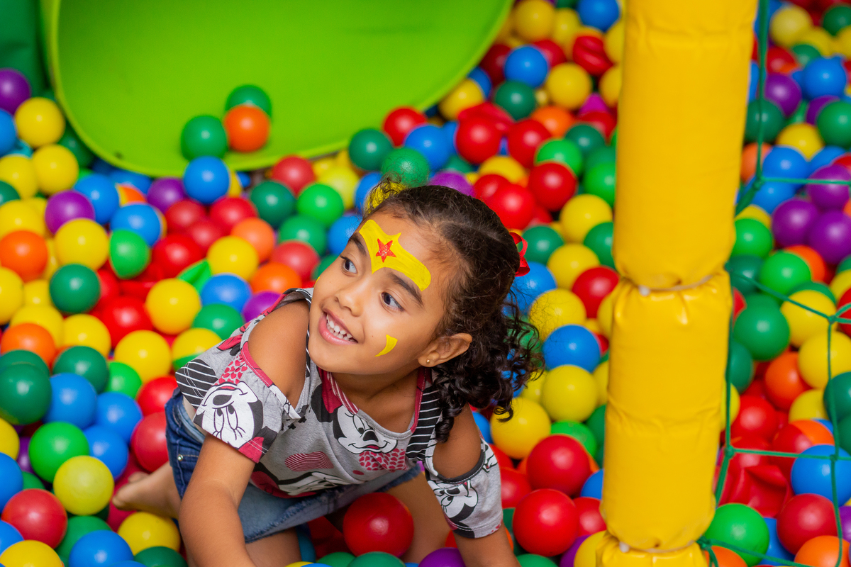menina de mulher maravilha brincando na piscina de bolinha