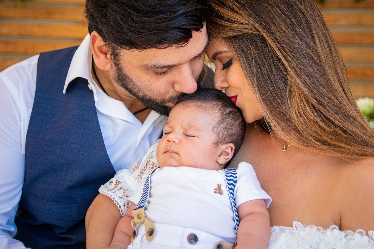 Mãe e pai dando um beijo no filho no dia de seu batismo