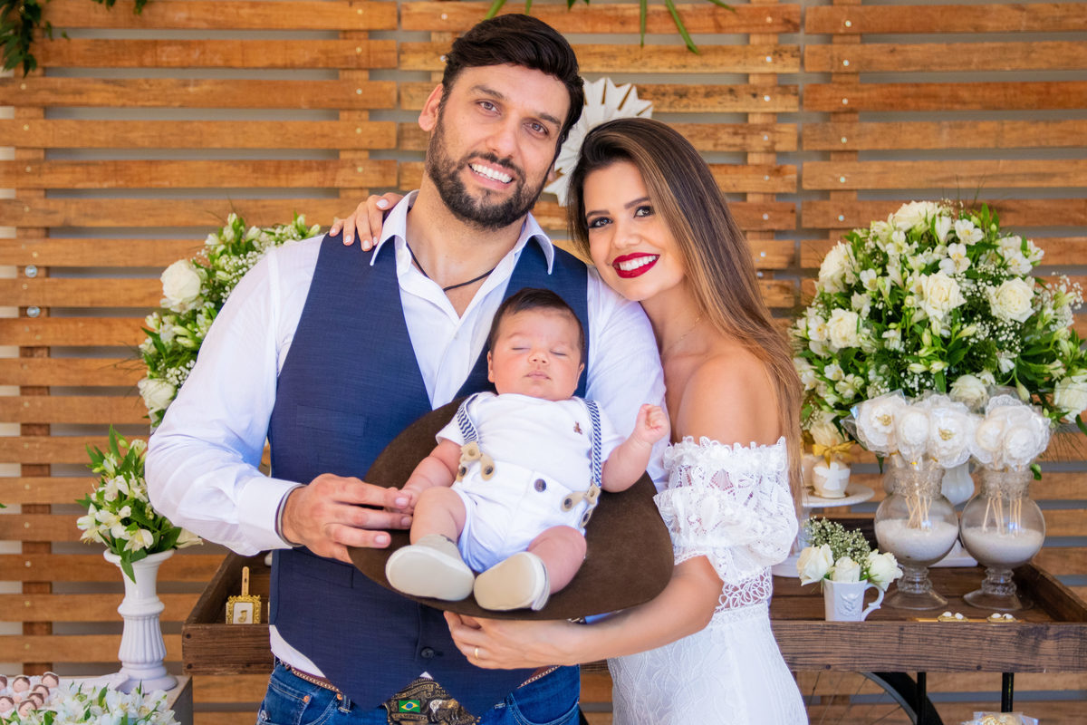 Nenê dentro do chapéu de cowboy, pai e mãe tirando foto com o filho no dia do batismo