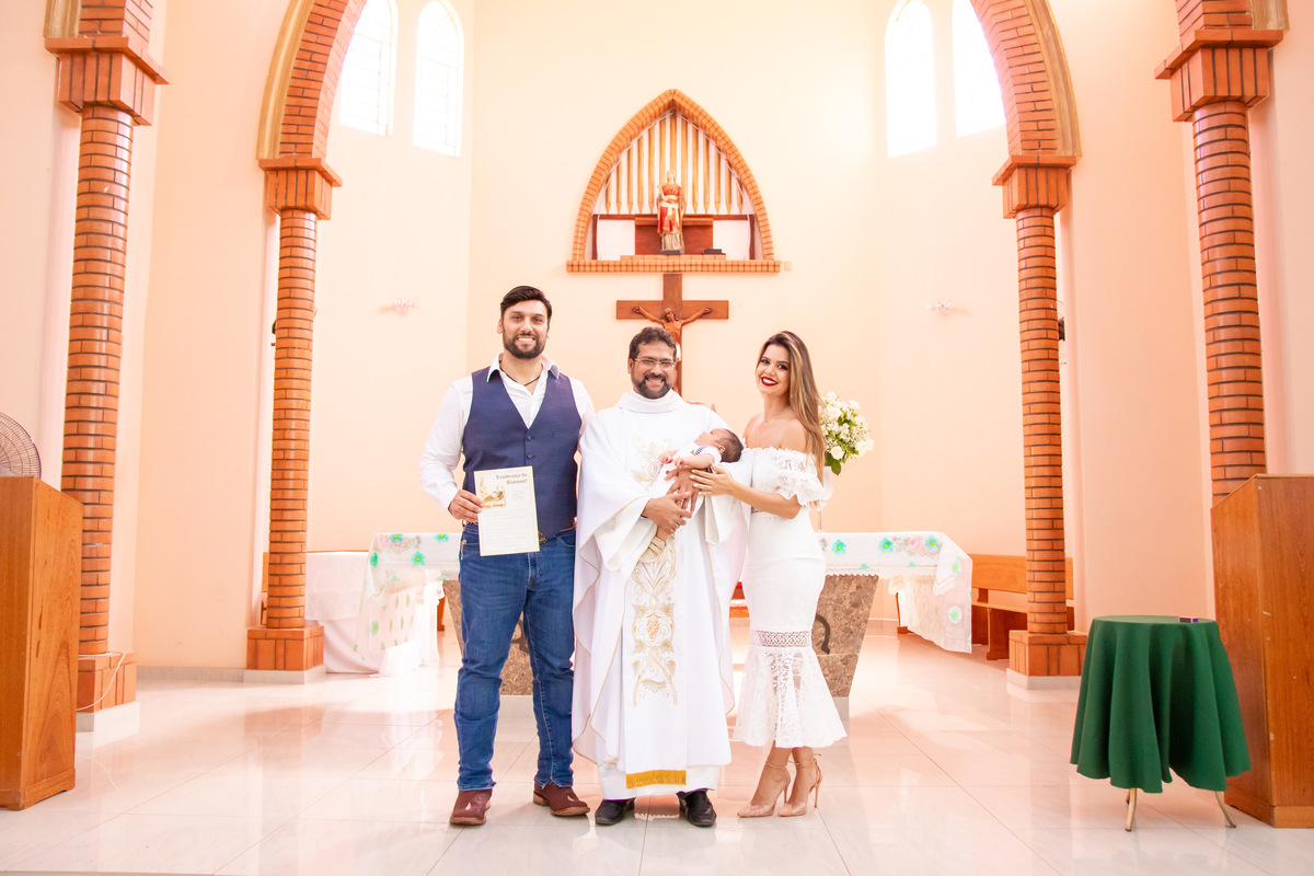 Pai, mãe, filho e padre sorrindo para a foto no batismo