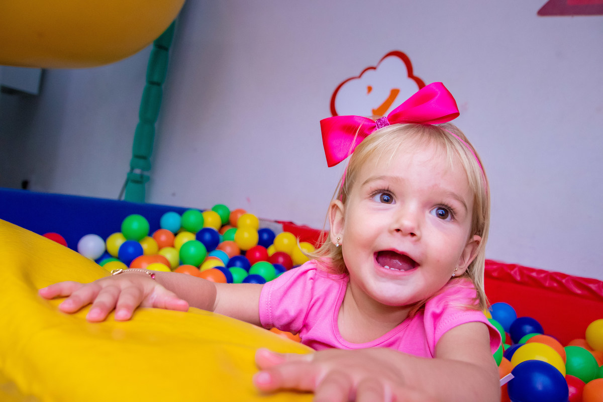 Buffet Pipoca Bauru, criança de laço rosa sorrindo na piscina de bolinhas