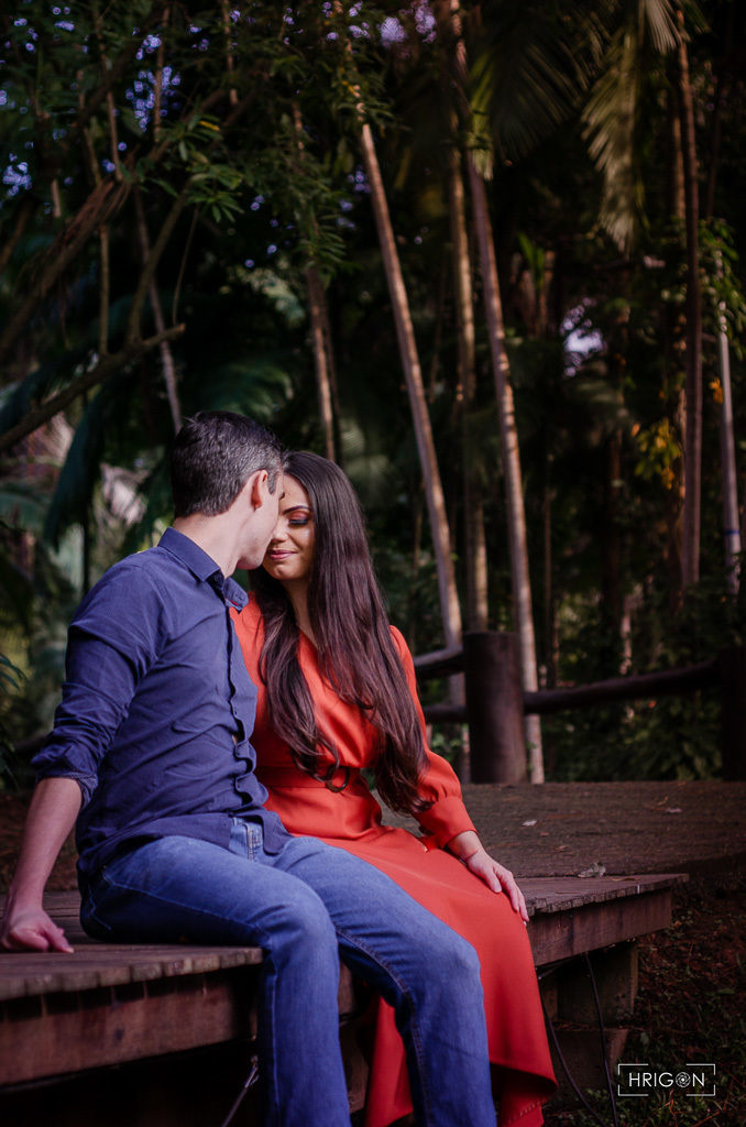 casal sentado na ponte juntando testa com testa de olhos fechados com árvores ao fundo