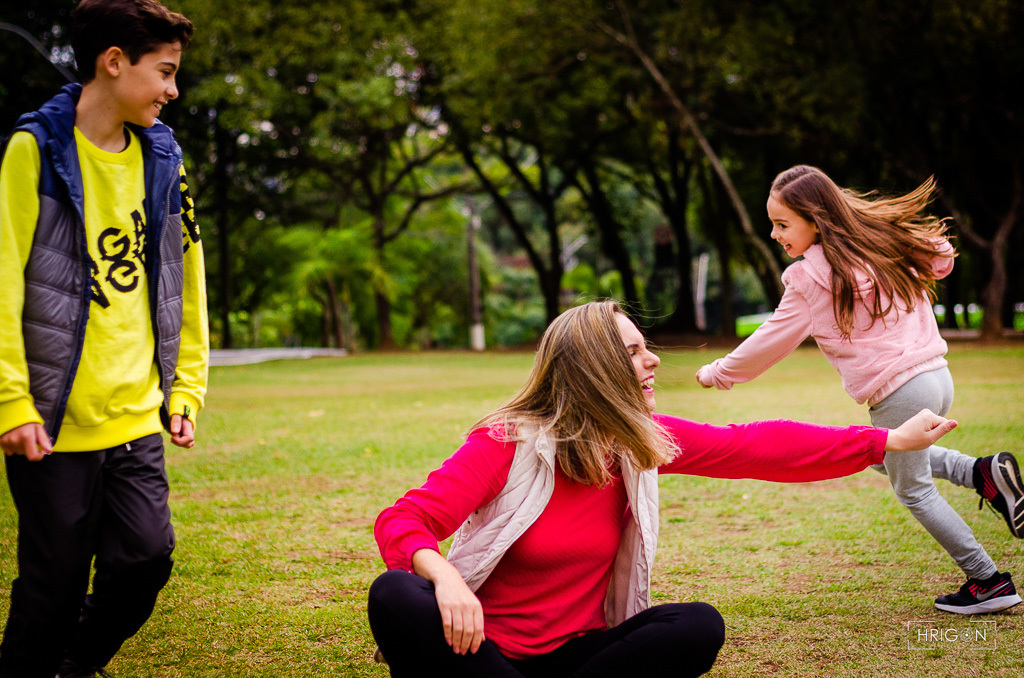 os filhos correndo ao redor da mãe que está sentada no chão. a mãe estica a mão para tentar alcançar a filha