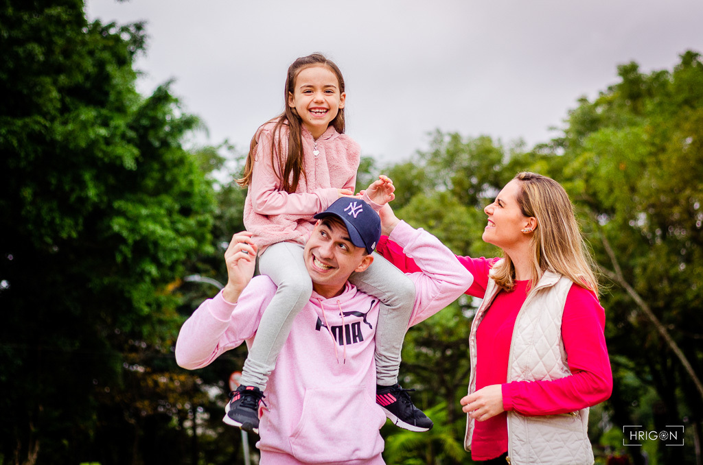 o pai está coma filha sobre os ombros e a mãe tentando fazer cócegas na filha