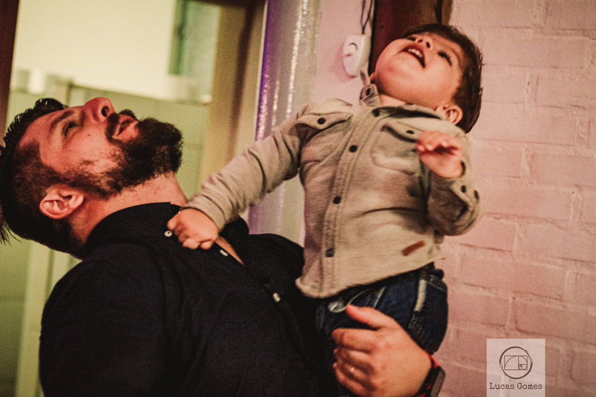  Fotografia Filho no colo de seu pai com a cabeça para cima em festa de debutante 