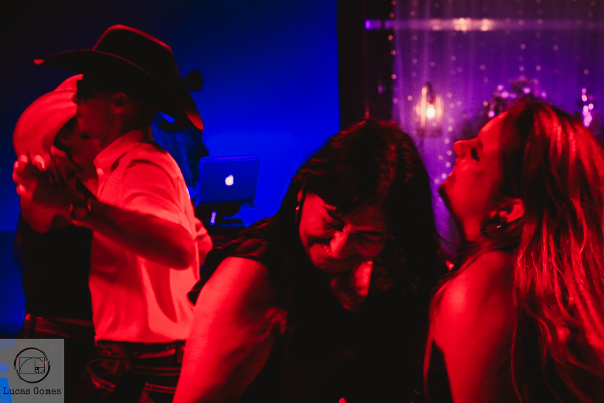 Fotografia de duas pessoas dançado em segundo plano, enquanto outras duas dão risada em primeiro plano  em festa de debutante 