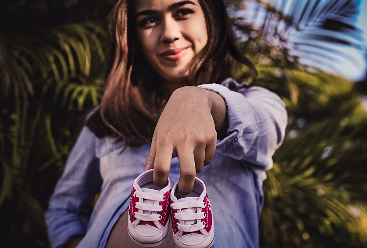 fotografia da gestante sorrindo  e segurando o tenis nos dedos de frente e sorrindo