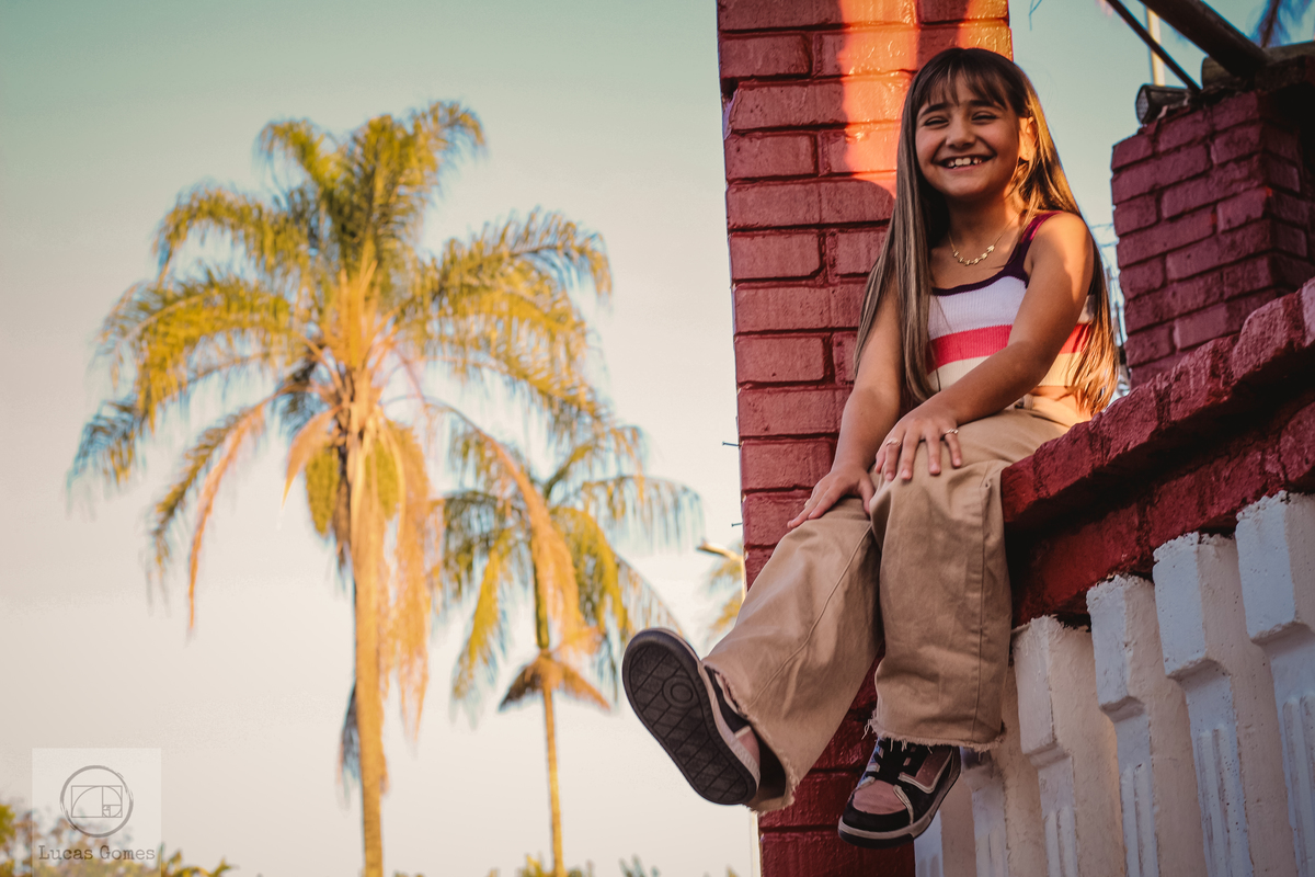 Fotografia da menina sentada com 2 palmeiras no fundo 