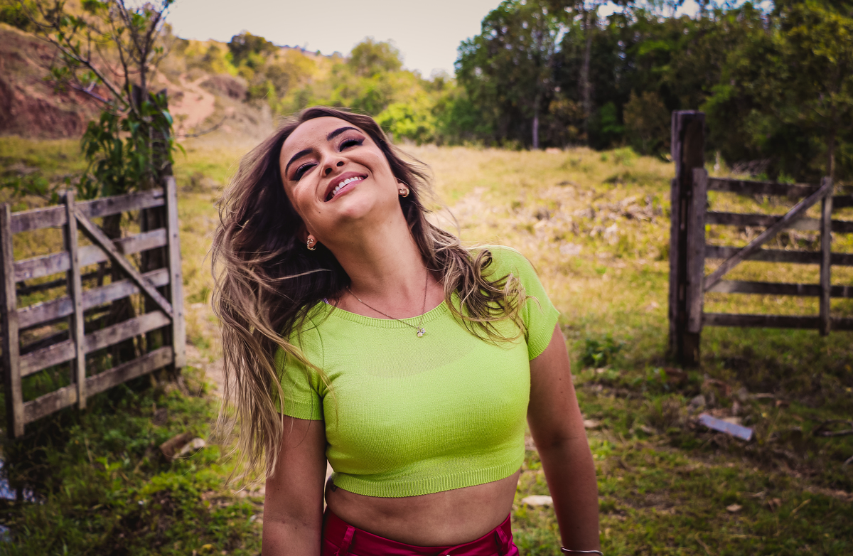 Fotografia de mulher jogando o seu cabelo e sorrindo com uma paisagem verde no fundo