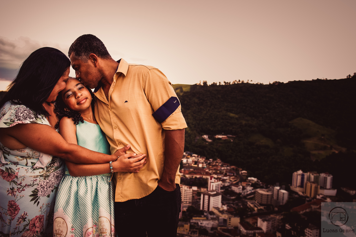 fotografia de pai e mãe beijando sua filha na cabeça