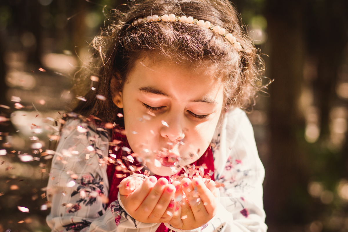menina assoprando papeis brilhantes ao vento