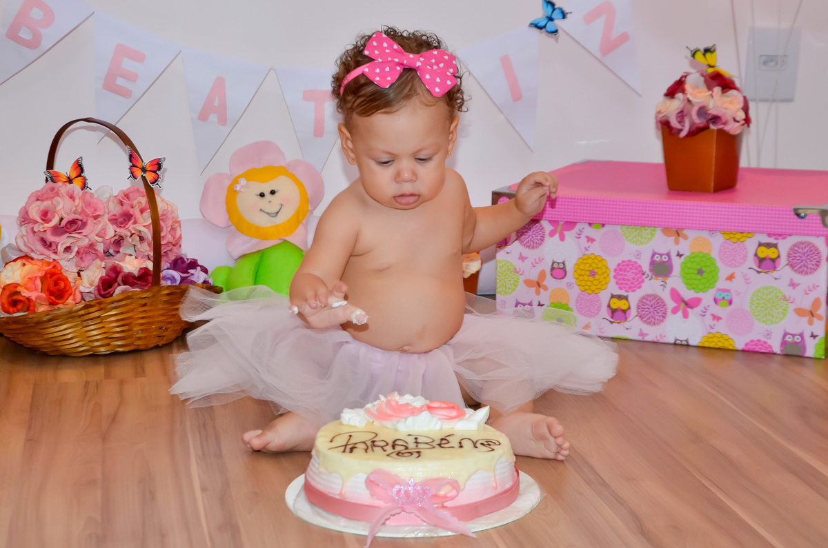 Foto de menina com tutu rosa em cenário com flores e bichinhos de pelúcia Assando um bolo de aniversário 