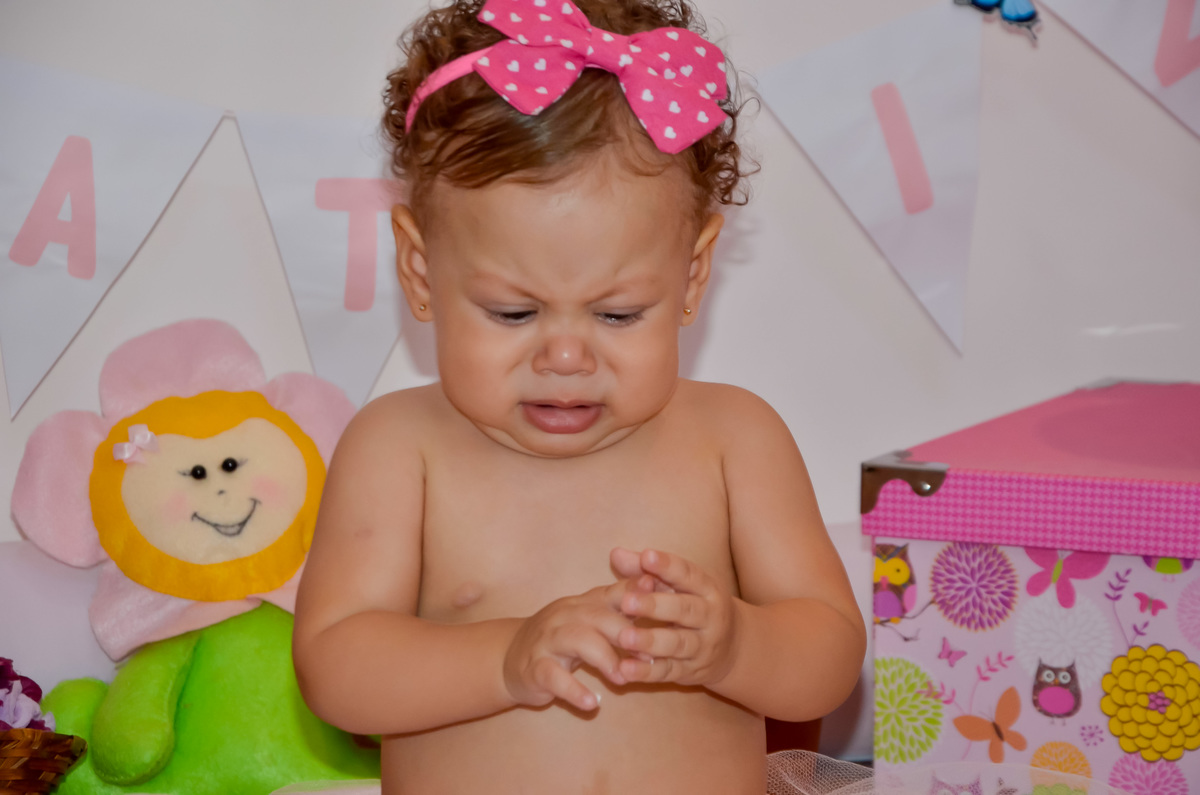 Foto de menina em cenário com flores e bichinhos de pelúcia fazendo careta