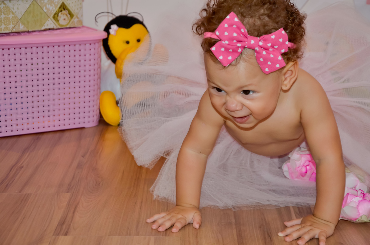 Foto de menina engatinhando e sorrindo em cenário com flores e bichinhos de pelúcia 
