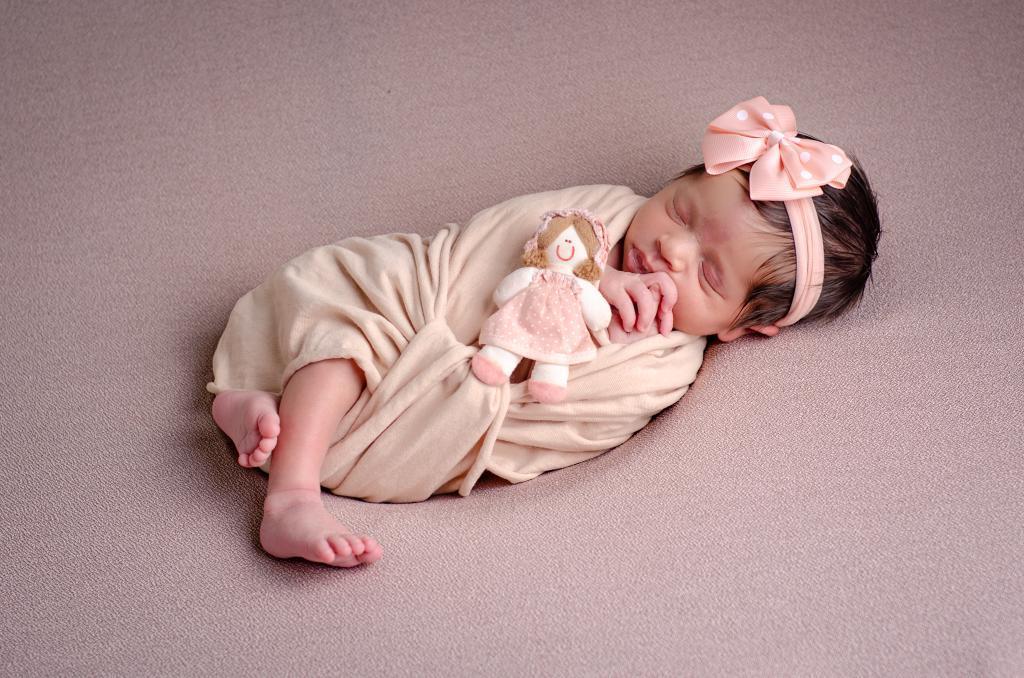 foto bebe menina dormindo newborn enrolada wrap segurando boneca de pano 