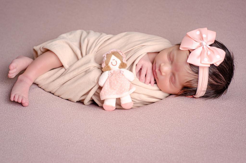 foto bebe memina dormindo newborn enrolada wrap segurando boneca de pano 