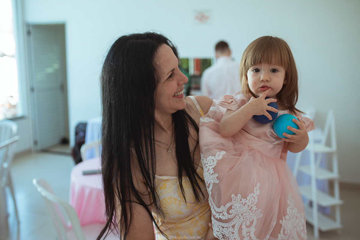 Fotografia espontânea da mãe abraçando a filha durante a comemoração do aniversário infantil.