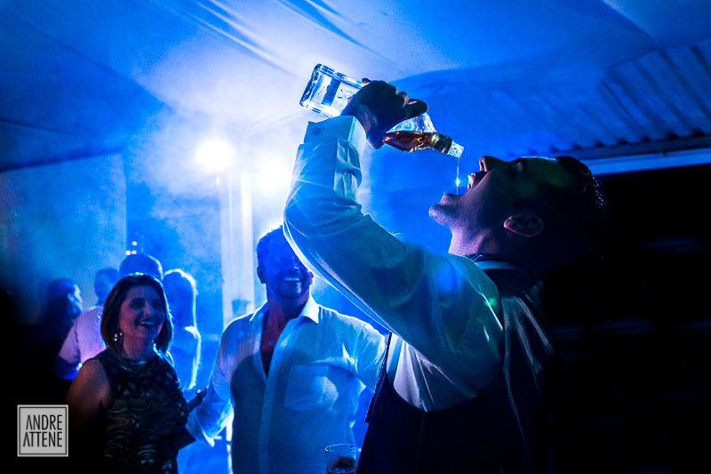 noivo bebendo em sua festa de casamento e convidados olham animados em fotografia de Andre Attene