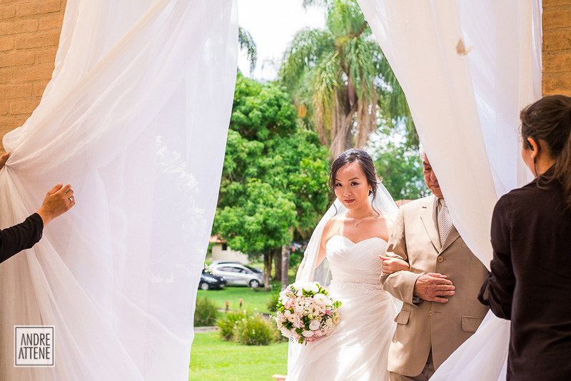 a cortina se abre e revela a noiva que chega com seu pai na cerimônia de casamento fotografada por Andre Attene