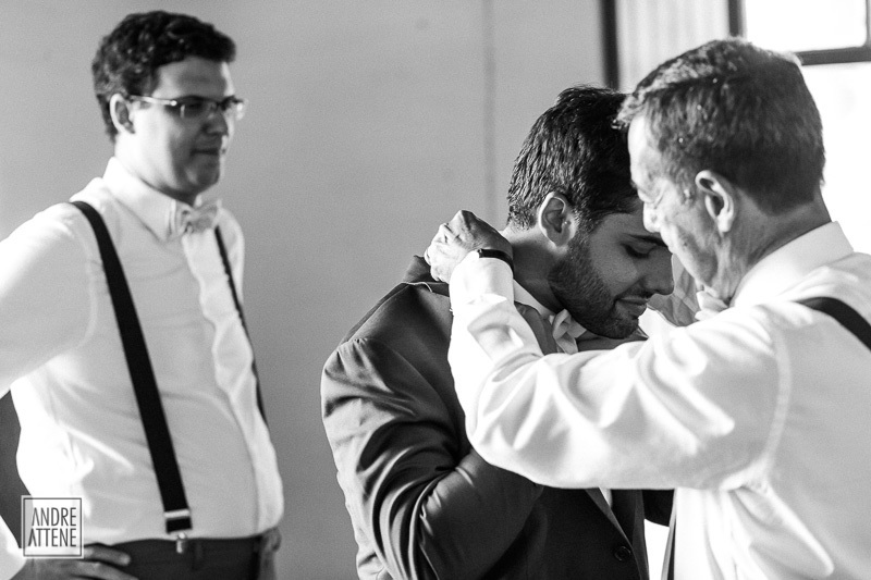 o pai do noivo o ajuda a se arrumar, enquanto seu irmão os observa emocionado