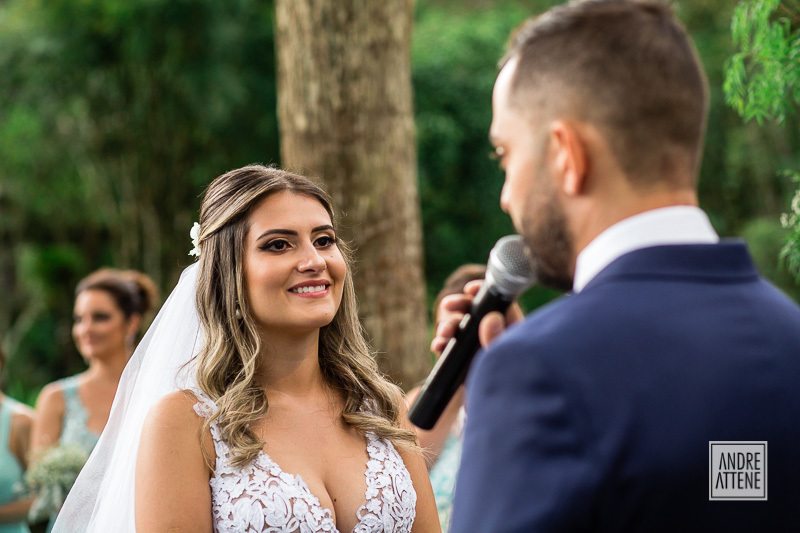 a noiva sorri emocionada enquanto ouve os votos de seu noivo