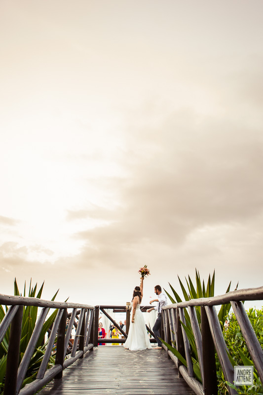 noiva acena com bouquet na mão muito feliz em seu casamento na praia fotografada com seu noivo por Andre Attene