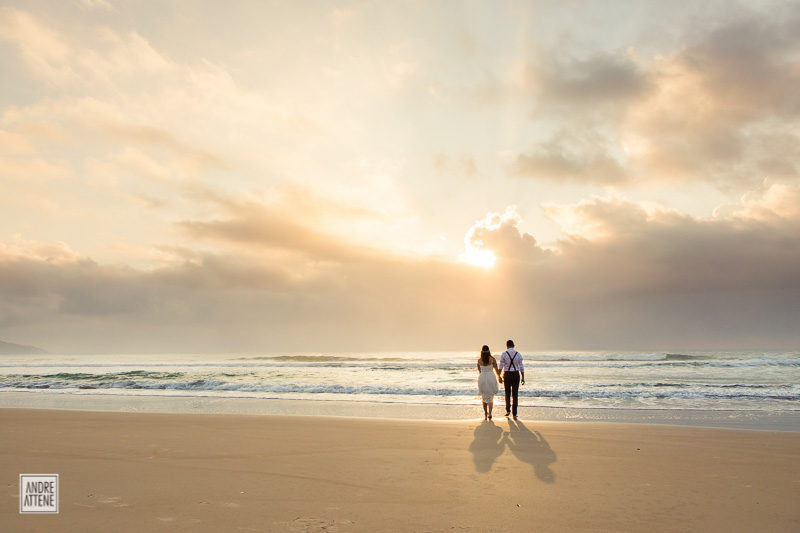 noivos de mãos dadas em seu casamento na praia admiram o horizonte em fotografia de Andre Attene
