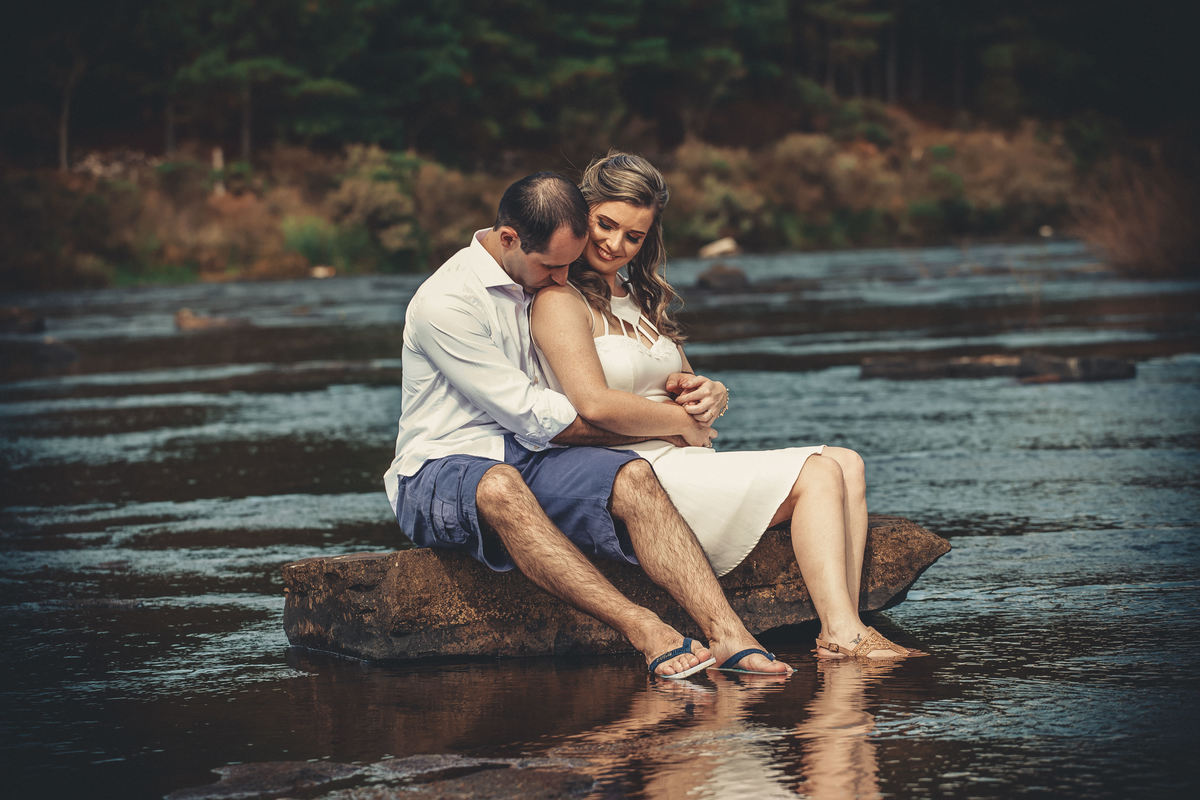 Fotógrafo de casamento de Cachoeirinha fotografia ensaio pré casamento casal sentado na pedra na beira do rio ele beijando o ombro dela