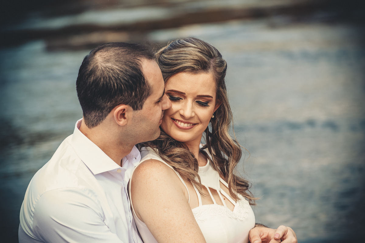Fotógrafo de casamento de Cachoeirinha fotografia ensaio pré casamento casal sentado na pedra na beira do rio ele beijando o rosto dela