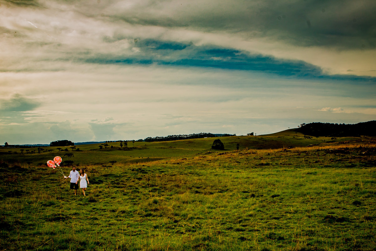 Fotógrafo de casamento de Cachoeirinha fotografia ensaio pré casamento casal de mãos dadas segurando os balões e caminhando no campo