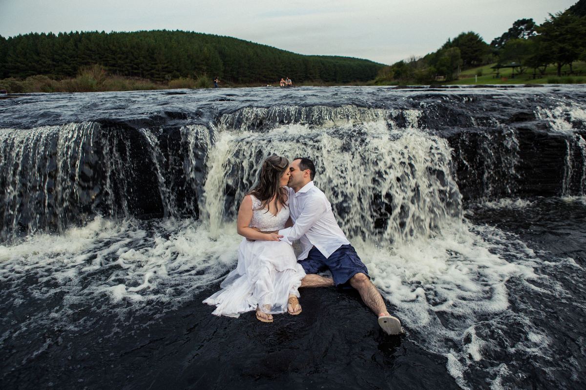 Fotógrafo de casamento de Cachoeirinha fotografia ensaio pré casamento casal sentado na pedra em frente a cachoeirinha se beijando