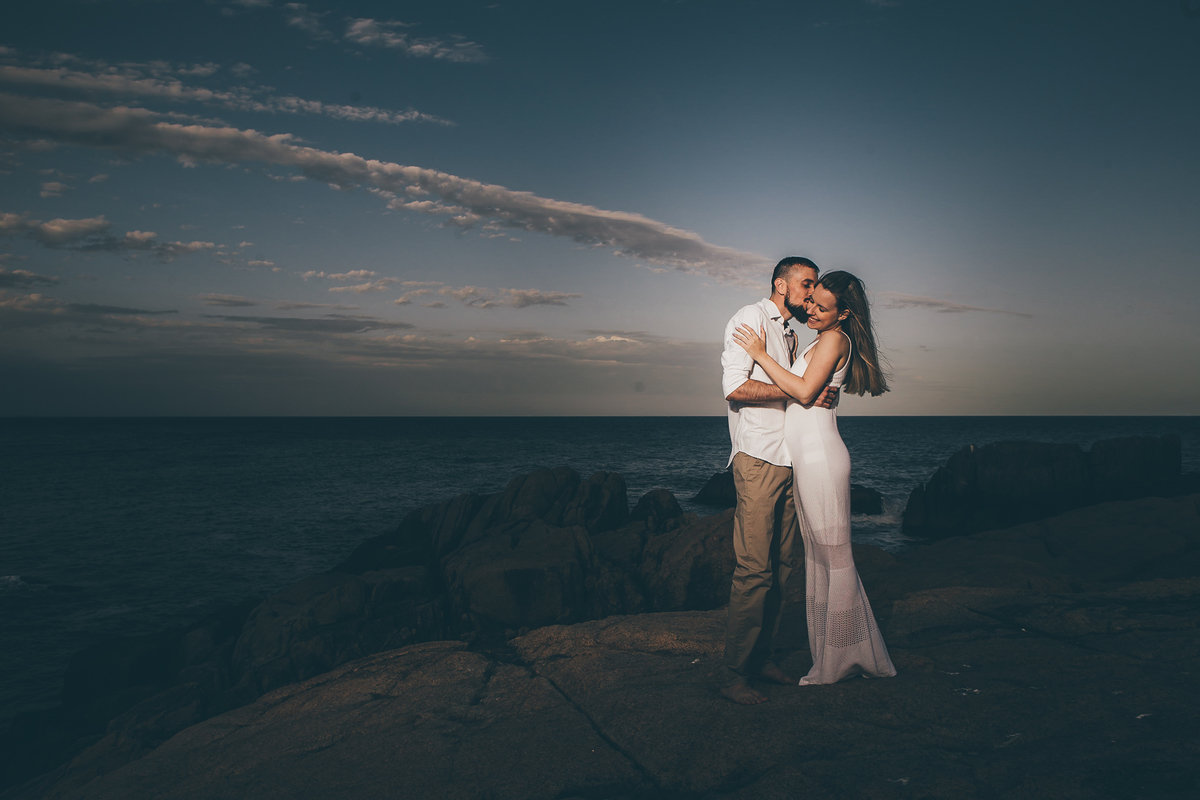 Fotógrafo de casamento de Cachoeirinha fotografia ensaio pré casamento casal nas pedras e o mar ao fundo ele beijando ela