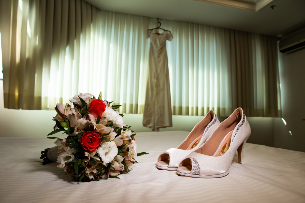 fotógrafo de casamento em cachoeirinha e porto alegre fotografia do sapato e do bouquet com o vestido da noiva ao fundo