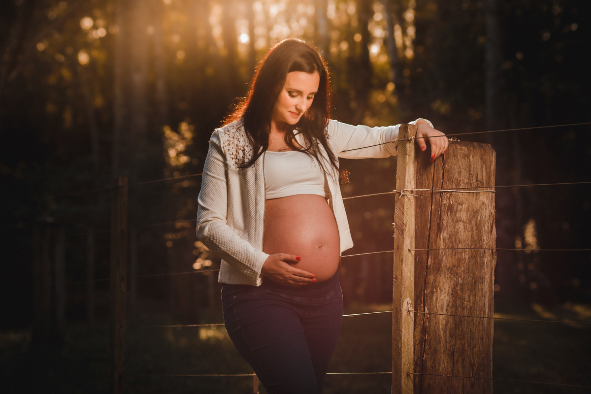 book de gestante com gestante em contra luz escorada num poste