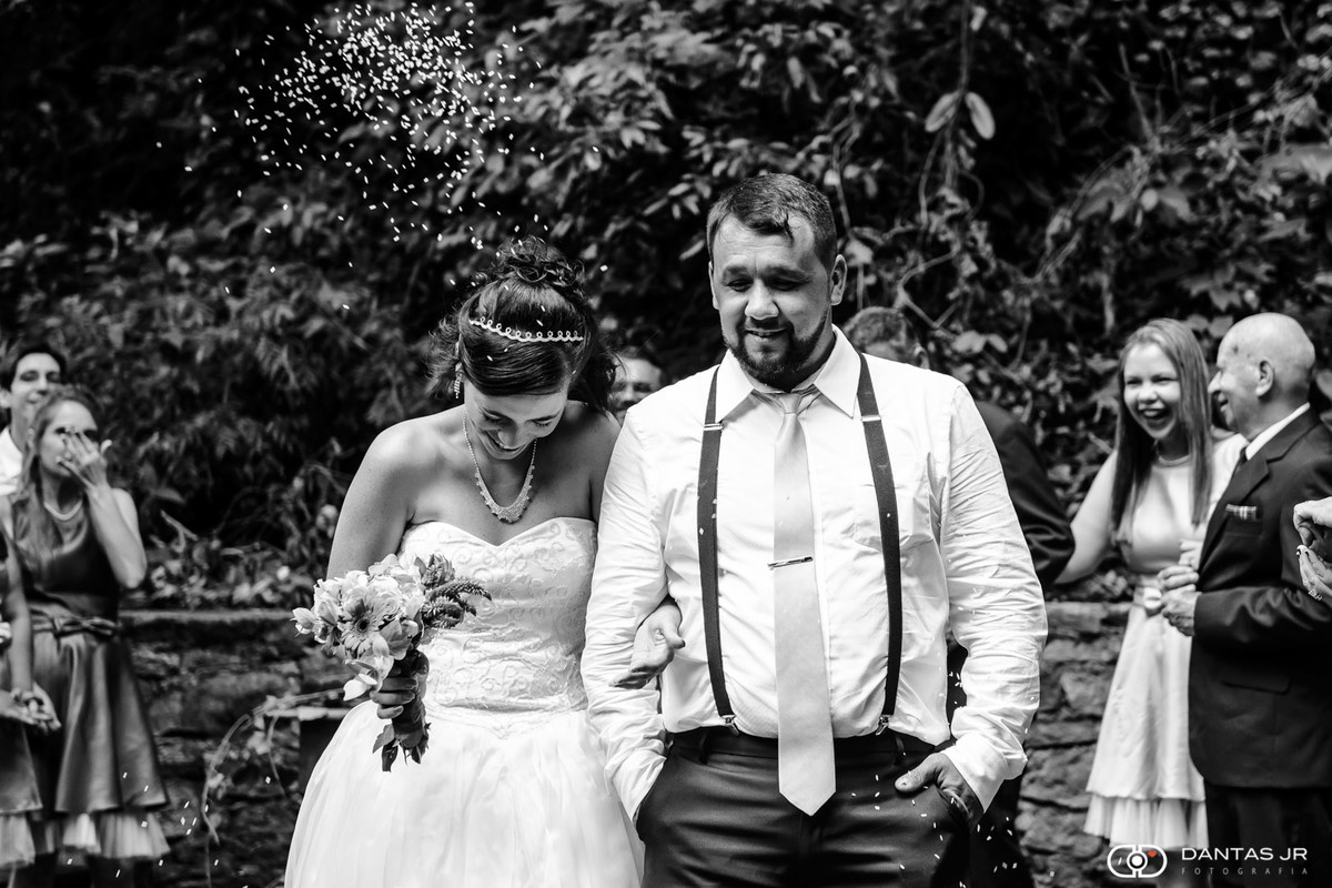 casal de noivos saindo da cerimônia de casamento ao ar livre com convidados jogando arroz em foto preto e branco por Dantas Jr. Fotografia