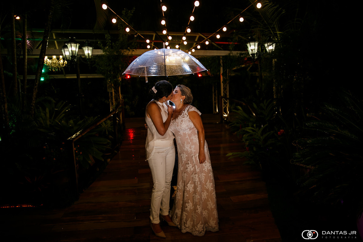 Casal de melheres noivas lésbicas em casamento homoafetivo no Bistrô 160 em Campo Grande RJ se beijando com guarda chuva debaixo de chuva pelo melhor fotógrafo de casamento Dantas Jr. Fotografia