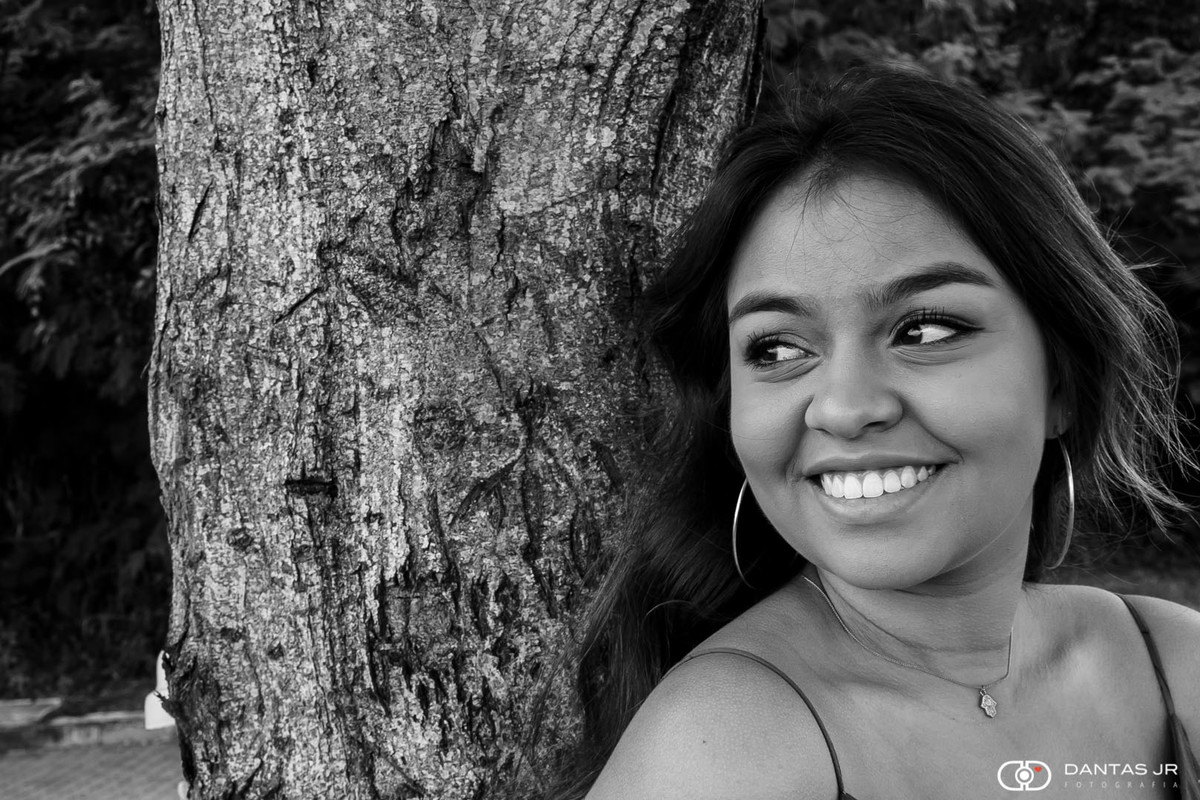 Menina encostada na árvore sorrindo em ensaio debutante por Dantas Jr. Fotografia