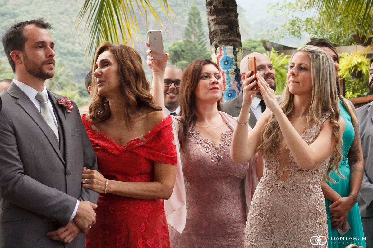 Noivo emoionado com convidados fotografando com celular observado pela mãe feliz em cerimonia de casamento judaico no solar das palmeiras na ilha da gigoia por Dantas Jr